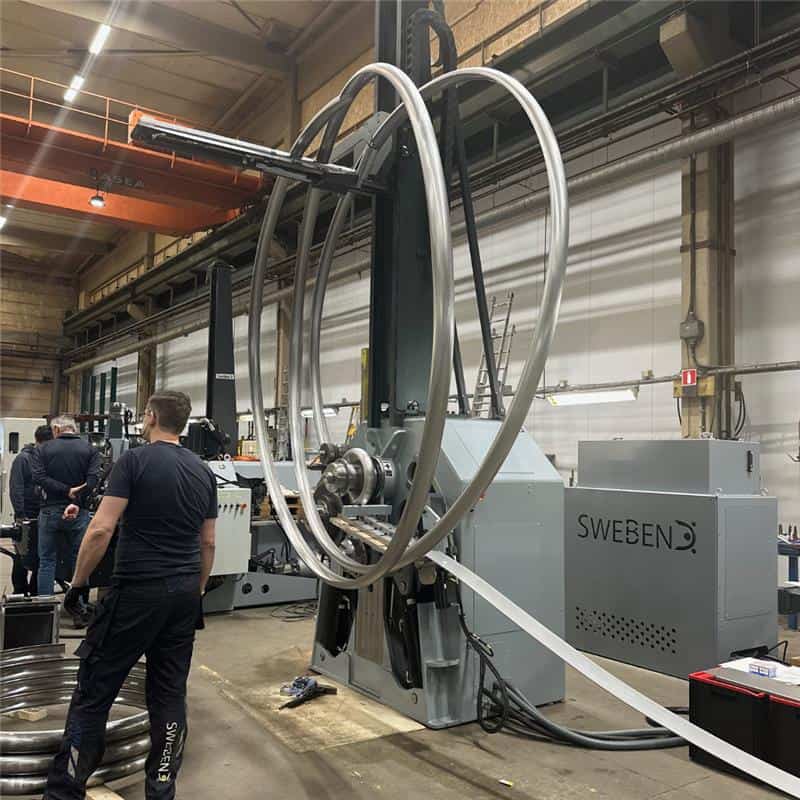 Engineer inspecting a large-diameter bent tube on an industrial tube bending machine by SweBend, showcasing advanced tube bending technology in a manufacturing facility.
