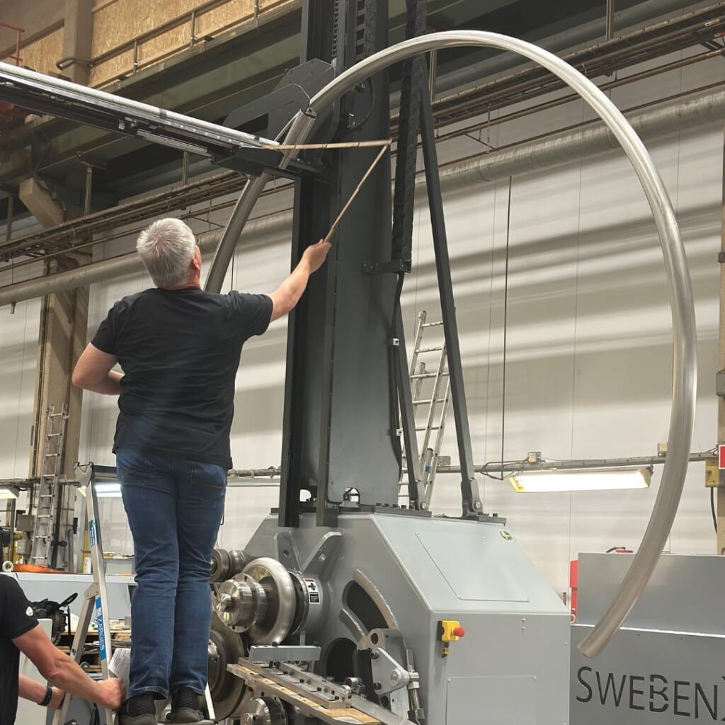 Multiple large stainless steel tubes being formed by a high-precision SweBend tube bending machine, illustrating cutting-edge tube bending technology in action on the factory floor.