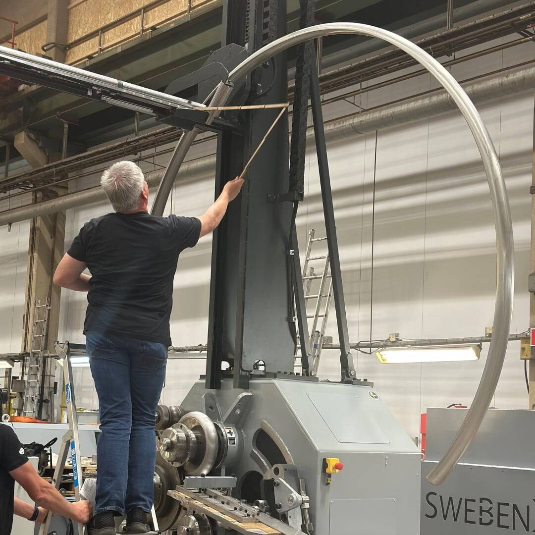 Multiple large stainless steel tubes being formed by a high-precision SweBend tube bending machine, illustrating cutting-edge tube bending technology in action on the factory floor.